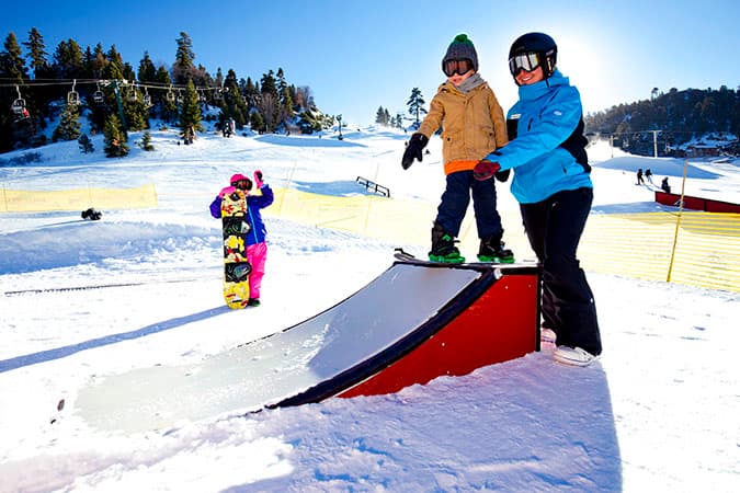 An instructor guiding a young rider over a skill-builder feature in the beginner park